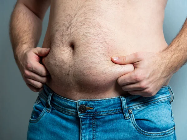 The man in jeans squeezes his hairy, flabby, fat stomach. The concept of poor nutrition. body positive. Self-acceptance