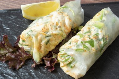 Siyah desenli bir tabakta yuvarlanmış börekler var. Arka planda taze limon. Lezzetli bir diyet. Asya mutfağı