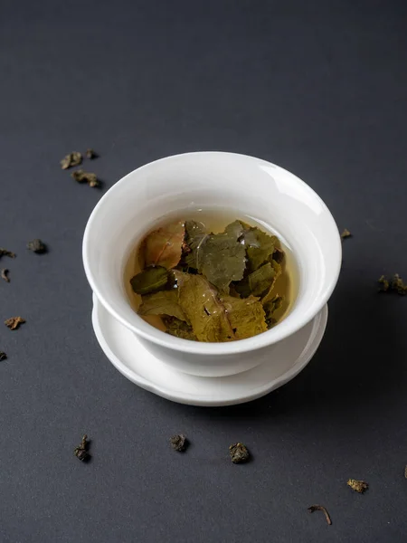 a white bowl with brewed tea leaves on a dark background. Close up, side view. Chinese tea, open leaves. vertical photo