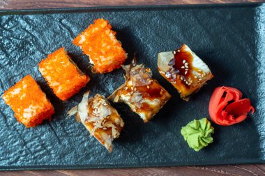 Suşili yemek kompozisyonu. Siyah tabakta, zencefil ve wasabi turşusunun yanında çeşit çeşit suşi. Üst manzara, düz uzanma