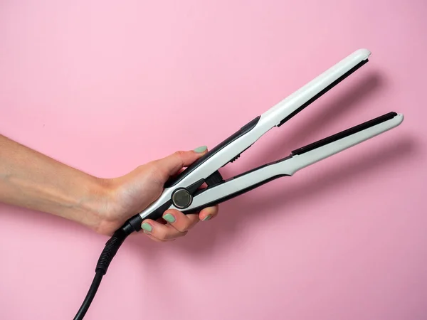 White curling iron in a woman\'s hand on a pnk background. An accessory for creating hairstyles. Beauty and fashion. Hair care.