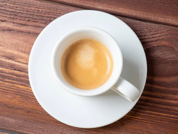 Ahşap zemin üzerinde taze demlenmiş espresso olan beyaz bardak. Üst manzara, düz yatış, kahverengi köpük. Kahve konsepti