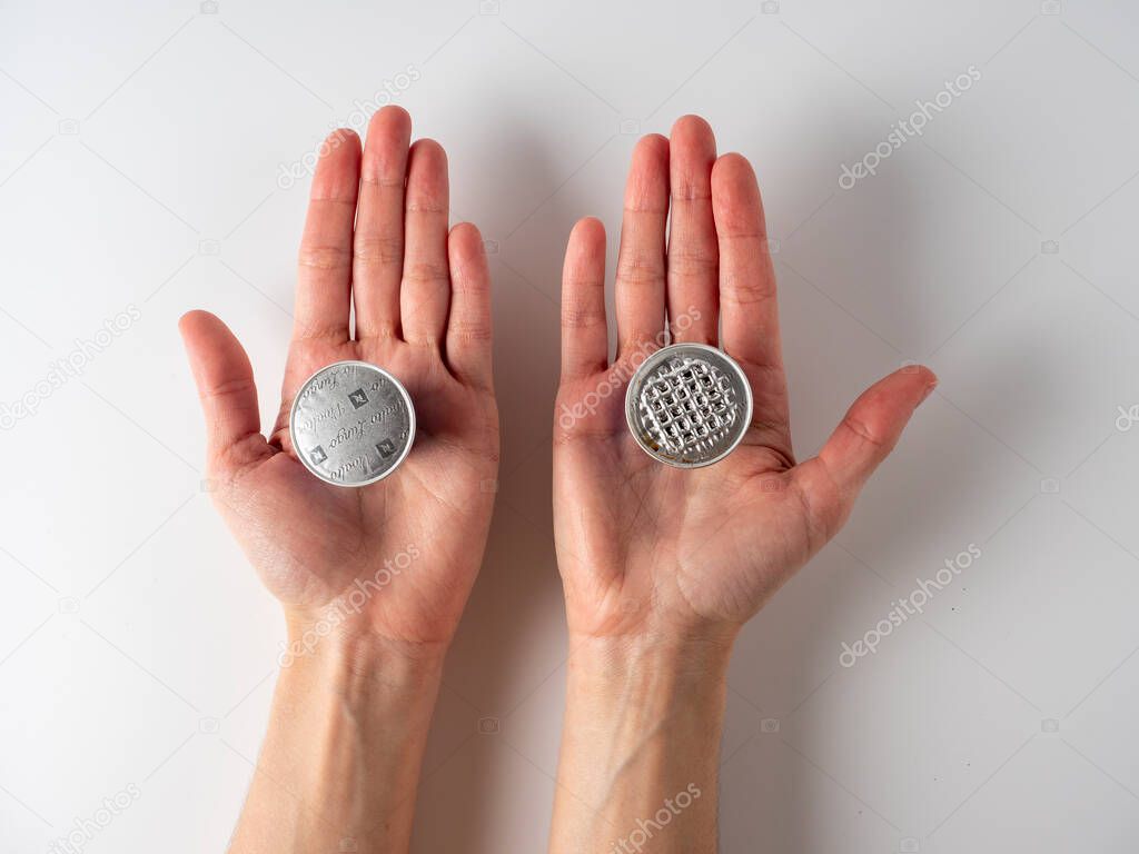 I10.03.2021 Russia, Moscow. n his hands are two aluminum capsules with ground Nespresso coffee . One of them is used. White background, top view, flat lay. The concept of recycling used items