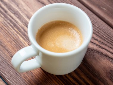 Ahşap zemin üzerinde lezzetli ve aromatik bir espresso olan beyaz bir fincan. yan görünüm