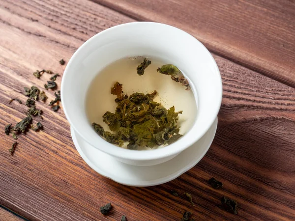 绿茶是在木制背景的白碗中酿制的 干茶叶子就在附近 顶部视图 — 图库照片