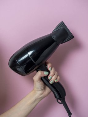 Pembe arka planda bir kadının elinde siyah saç kurutma makinesi. Saç bakım ürünleri. Dikey fotoğraf