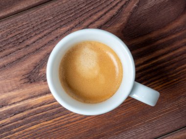 Beyaz bir fincanda, ahşap bir arka planda güzel kokulu bir kahvenin yakın çekimi. Kahverengi köpük, üst görünüm, düz uzanma