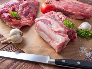 Birkaç parça taze çiğ et parşömen üzerine yayılır. Sarımsağın, otların, domateslerin ve bıçağın yanında. Yan görünüm.