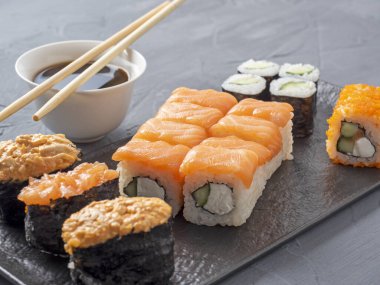 Philadelphia suşisi gri arka planda siyah desenli bir tabakta yuvarlanıyor. Yakınlarda bambu çubukları var. Yan manzara, Japon mutfağı.