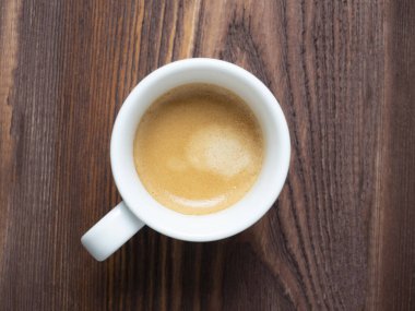 Beyaz bir fincanda, ahşap bir arka planda güzel kokulu bir kahvenin yakın çekimi. Kahverengi köpük, üst görünüm, düz uzanma