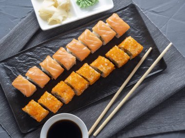 Philadelphia ve California 'yı siyah bir plakaya yuvarla. Üst manzara, düz yatış. Zencefil, wasabi ve soya sosu yakında. Geleneksel Japon mutfağı