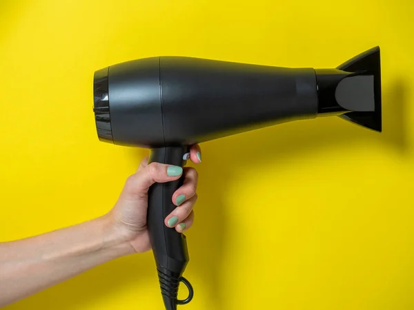 Mão de menina segurando o secador de cabelo.