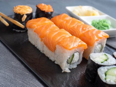 çeşitli Japon dürümleri ve dokulu bir tabakta suşi. Yan görüş. Yakınlarda zencefil ve sos çubukları var..