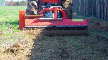 Çit boyunca çim biçme makinesi olan bir traktör. Arazi çizimi işleniyor