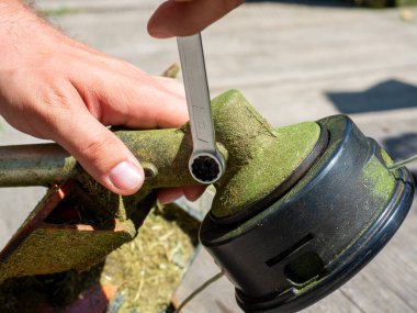 Çim biçme makinesinin yakın plan çekiminde vites kutusundaki vida İngiliz anahtarıyla sökülmüş. Ekipmanların bakımı, vites kutusunun yağlanması.