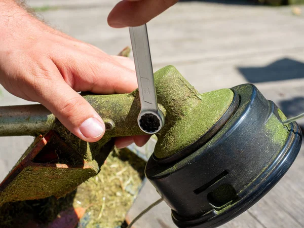 Çim biçme makinesinin yakın plan çekiminde vites kutusundaki vida İngiliz anahtarıyla sökülmüş. Ekipmanların bakımı, vites kutusunun yağlanması.