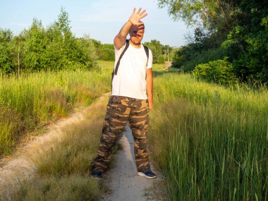 Bir adam ormanın içinde güneşe bakan bir yolda duruyor ve eliyle ışığı engelliyor. Yüzünde bir elin gölgesi. Seyahat ve dinlenme konsepti