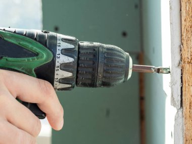 Bir adam bir tornavida tutuyor ve vidayı alçıpana sıkıştırıyor. seçici odak