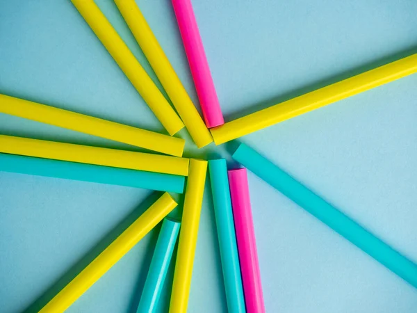 Multicolored plastic tubes are laid out on a blue paper background. Top view, flat lay