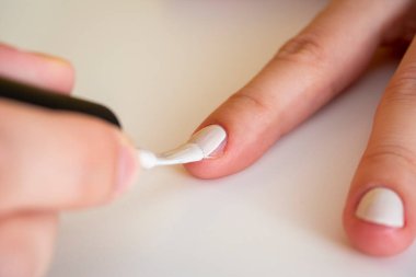 Bir fırçayla beyaz tırnak cilası sürmeye yakın çekim. Evde manikür. Kalitesiz manikür.