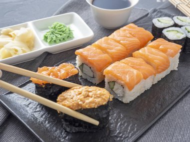 çeşitli Japon dürümleri ve dokulu bir tabakta suşi. Yan görüş. Yakınlarda zencefil ve sos çubukları var..