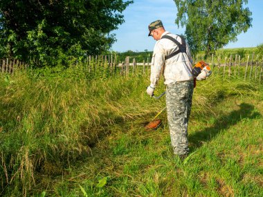 Benzin biçme makinesi kullanan bir adam uzun otlar keser. Yaz. Kırsal alan, bölgenin bakımı.