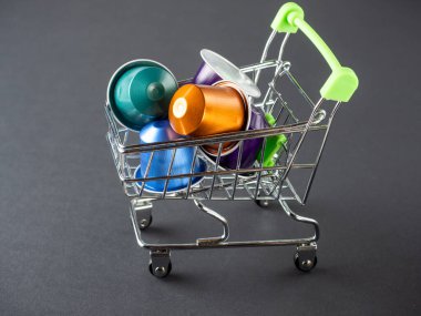 Aromatik öğütülmüş kahveyle dolu renkli alüminyum kapsüllerle dolu küçük bir market arabası. Modern kahve depolama ve hazırlama teknolojileri. Siyah arkaplan.