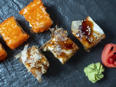 Suşili yemek kompozisyonu. Siyah tabakta, zencefil ve wasabi turşusunun yanında çeşit çeşit suşi. Üst manzara, düz uzanma