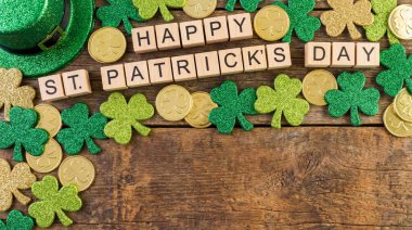 Aziz Patrick Günü 'nde ahşap harflerle çevrili yeşil yonca ve altın sikkelerle çevrili Mutlu Aziz Patrick Günleri sahnesi..