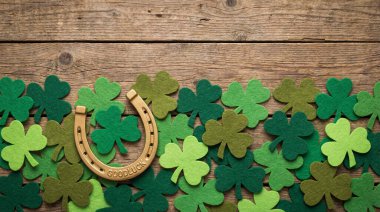 Aziz Patrick Günü sahnesinde yıpranmış ahşap bir yüzey üzerinde yeşil yonca ile çevrili altın bir at nalı var..