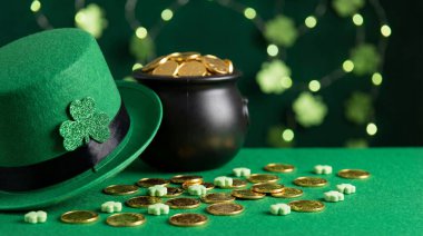 Bir leprikon şapkalı, altın paralarla dolu bir çömlek ve yeşil bir yüzeye saçılmış yoncalar içeren şenlikli bir Aziz Patrick Günü sahnesi..