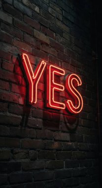 Canlı kırmızı neon bir tabela EVET, koyu renkli tuğla bir duvara karşı parlak bir şekilde parlar, çarpıcı bir kontrastlık ve loş ışıklı bir ayarda cesur bir ifade yaratır.