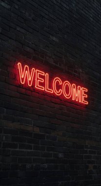 Çarpıcı kırmızı neon bir tabela hoş geldin diyor koyu renkli tuğla bir duvara karşı parlıyor loş ışıkta sıcak ve davetkar bir atmosfer yaratıyor..