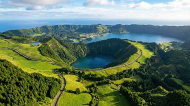 Bir hava görüntüsü, Azores, Sao Miguel Adası 'ndaki volkanik bir kraterin içine yerleştirilmiş, bir mavi ve bir yeşil Sete Cidades ikiz göllerini yakalar. Çevresindeki manzara, yuvarlanan yeşil tepeler, sık ormanlar ve dolambaçlı ro 'dan oluşan canlı bir duvar halısıdır.