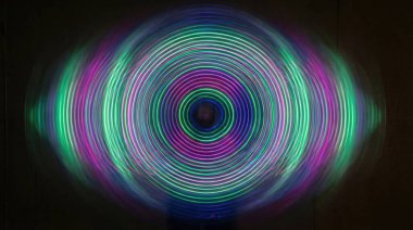 Bir LED dönen oyuncağın büyüleyici uzun pozlama çekimi, büyüleyici dairesel ışık desenleri üreterek karanlık bir arkaplana karşı, hareket ve ışık sanatını çağrıştırıyor.