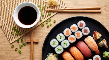 İçinde maki dürümleri ve nigiri bulunan nefis bir suşi çeşnisi, yanında da bir kase soya sosu, zencefil, wasabi ve bambu hasırının üzerinde yemek çubukları bulunan, ahşap bir masa..