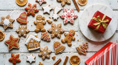 Ev yapımı zencefilli kurabiyelerden oluşan, beyaz kremayla süslenmiş, eskimiş beyaz ahşap bir yüzeye yerleştirilmiş enfes bir kare. Altın kurdeleli küçük kırmızı bir hediye kutusu yuvarlak beyaz bir tahtanın üzerinde duruyor.