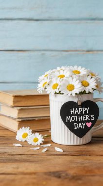 Kalp şeklinde Mutlu Anneler Günü etiketi ile süslenmiş, açık mavi arka planı olan, kırsal ahşap bir masanın üzerindeki eski kitap yığınına karşı kurulu, taze papatyalarla dolu beyaz bir kupanın yer aldığı büyüleyici bir hayat..
