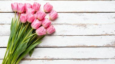 Güzel bir buket taze pembe lale taşralı beyaz ahşap bir masanın üzerinde duruyor, bahar ve kutlamalar için mükemmel canlı ve zarif bir görüntü yaratıyor..
