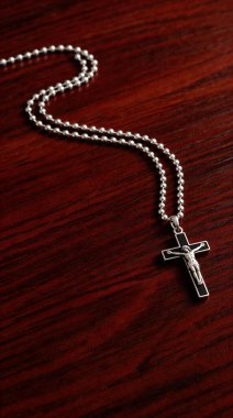 Üzerinde ayrıntılı bir İsa figürü bulunan gümüş bir haç kolyesi zengin, karanlık bir tahta yüzeye dayanır. İnanç, maneviyat ve dini bağlılık temalarını vurgular..