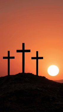 Üç haçtan oluşan güçlü bir siluet, bir tepenin üstünde canlı turuncu bir günbatımına karşı duruyor. İnanç, fedakarlık ve maneviyat temalarını çağrıştırıyor..