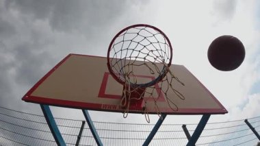 Basketbol, kapalı gökyüzüne karşı kapalı bir perspektifle çemberden geçiyor. Yüksek kaliteli FullHD görüntüler