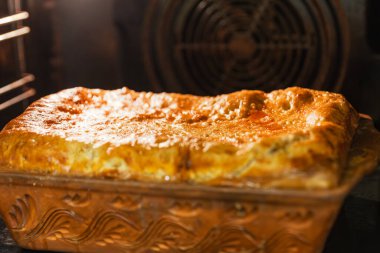 Mükemmel kaşarlanmış, çıtır çıtır altın hamurlu ev yapımı bir turtanın detaylı bir fotoğrafı. Hamur işi bir fırının içinde geleneksel bir kil tabakta pişirilir. Yumuşak dokusunu ve lezzetli görünümünü ön plana çıkarır..