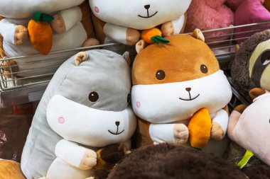 Yumuşak gri ve kahverengi hamsterların küçük peluş havuç ve meşe palamudu tutan doldurulmuş hayvanlarının yakın çekimi. Oyuncaklar tatlı gülümseyen yüzlere sahip ve çocukluk ve hediye temalı içerik için mükemmel bir perakende rafına yerleştirilmiş..