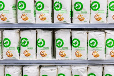 Markette 2 kg Auchan marka buğday unuyla dolu raflar. Yeşil kuş logosu olan beyaz kağıt çantalar bir hipermarketin pişirme malzemeleri bölümünde sıra sıra dizilmiş..