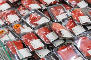 Yüksek açılı ham kırmızı sığır eti manzarası plastik tepsilerde vakumlu ve portakal rengi etiketlerle kapatılmış, hipermarkette sergilenen, perakende gıda satışlarını, market alışverişini ve et endüstrisini gösteren,.