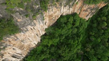 Tayland 'ın Koh Hong adasındaki bir kireçtaşı dağının yukarıdan aşağıya doğru görüntüsü. İnsansız hava aracı aşağıdaki orman tepe örtüsüne doğru hareket ederek baş dönmesi yaratıyor..