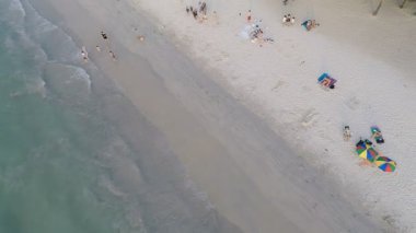 Aerial shot of tropical island beach with umbrellas white sand and people