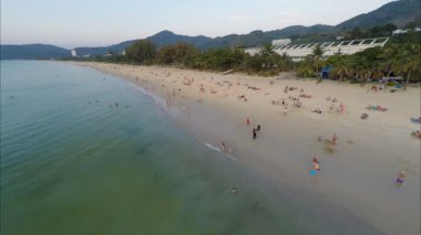 İnsanlar, dalgalar ve kumla dolu tropikal ada sahili.