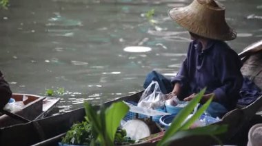 Tayland 'da yüzen bir markette kanodaki yaşlı Taylandlı kadın yemek yiyor ve satıyor.